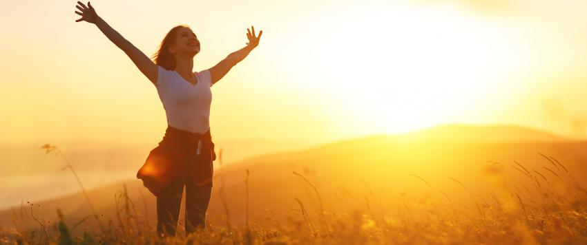 امرأة شابة تقف في حقل وترفع يديها في الشمس بسعادة